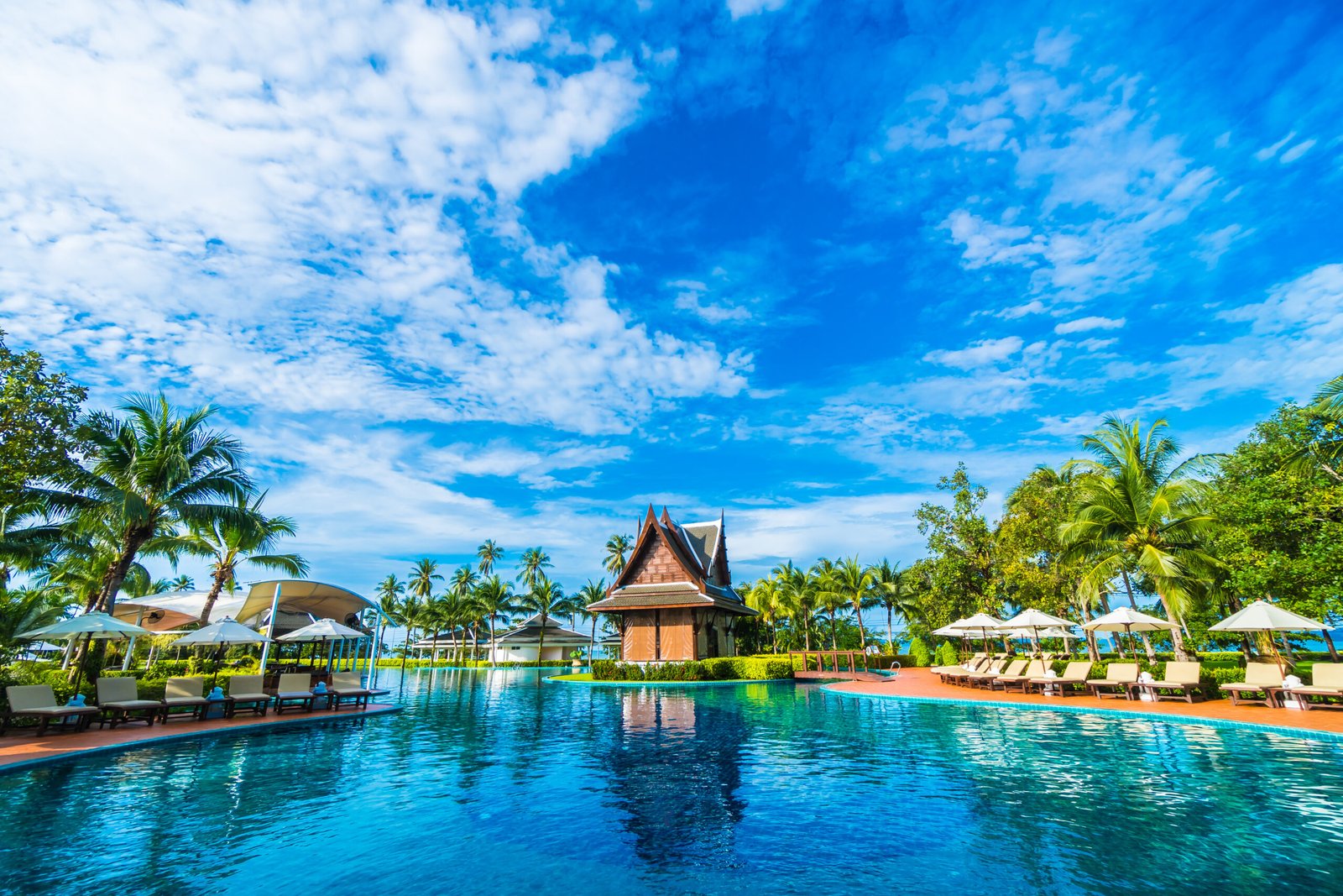 Beautiful luxury umbrella and chair around outdoor swimming pool in hotel and resort with coconut palm tree on blue sky - Boost up color Processing
